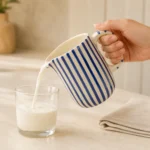 Blue striped ceramic jug being used to pour milk