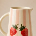 Close-up of the handpainted strawberry artwork and glossy glaze on a handmade ceramic water jug